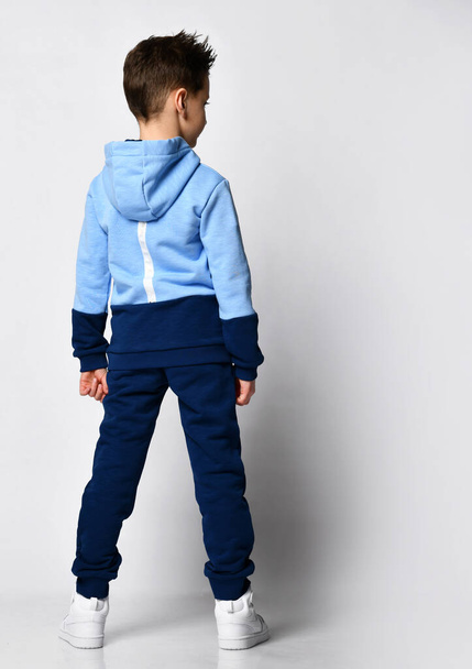 Kid in warm overalls, white sneakers walking along the studio wall. Full-length portrait. Childrens fashion, casual wear, comfortable children clothing for winter and autumn - 写真・画像