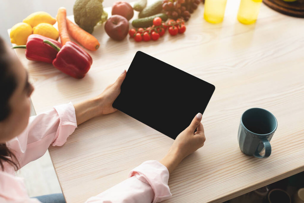 Mujer usando tableta con pantalla vacía para maqueta en la cocina - Foto, imagen