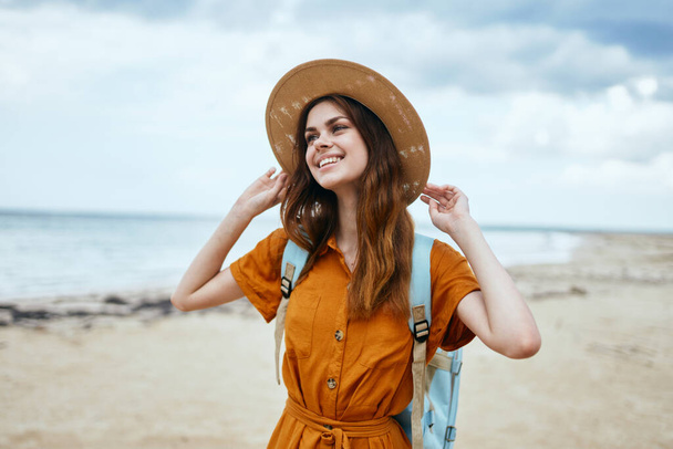 femme avec sac à dos marche sur la plage et chapeau robe de soleil voyage océan - Photo, image
