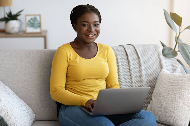 Freelance-ura. Onnellinen musta nainen kannettavalla tietokoneella kotona, nauttien etätyöstä - Valokuva, kuva