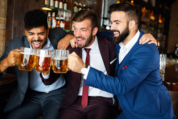 Handsome businessmen drinking beer, talking and smiling while resting at the pub - Foto, immagini