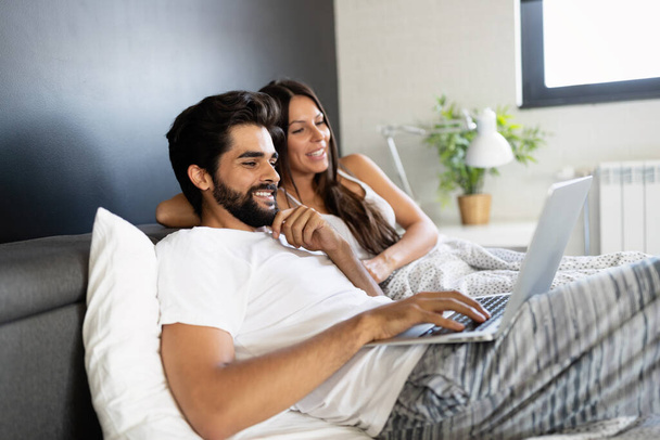 Young happy smiling couple with laptop at bedroom - Fotoğraf, Görsel