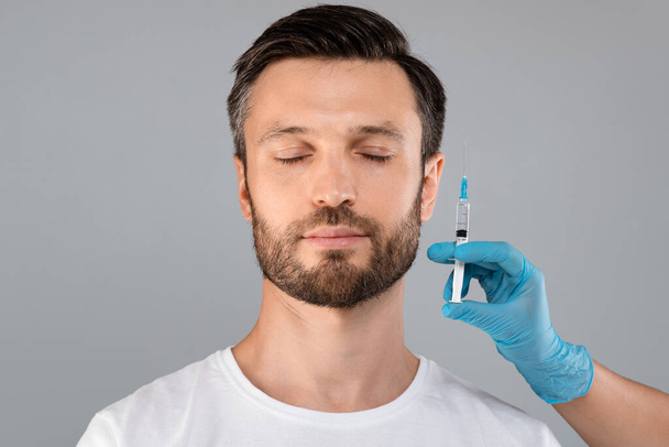 Γενειοφόρος άνδρας με κλειστά μάτια και χέρι γιατρού με σύριγγα - Φωτογραφία, εικόνα