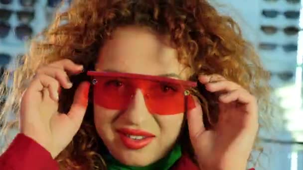 vrouw met bril shakes krullend haar en knipogen in studio - Video