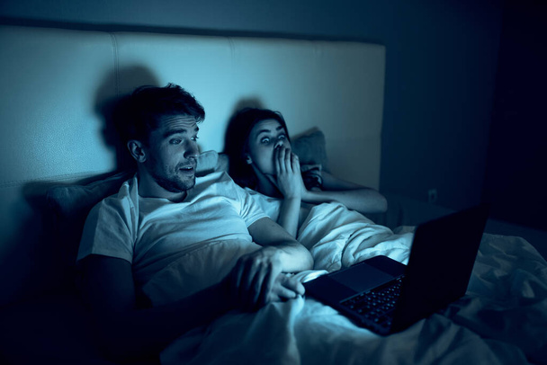 young couple lying on bed at night in front of laptop - Foto, Imagen