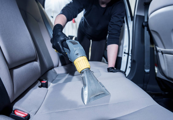 Worker cleans car interior with vacuum cleaner - Foto, Bild