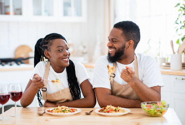 Huiselijke lunch. Gelukkig zwarte echtgenoten eten spaghetti en drinken wijn in de keuken - Foto, afbeelding