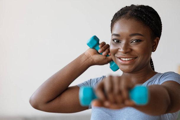 Упражнения дома. Спортивная афроамериканка, тренирующаяся с гантелями - Фото, изображение