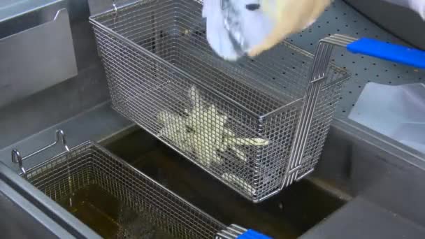 Frying fresh or frozen french fries in a professional looking frying basket submerging by bubbling, boiling hot frying oil. Static camera. - Footage, Video