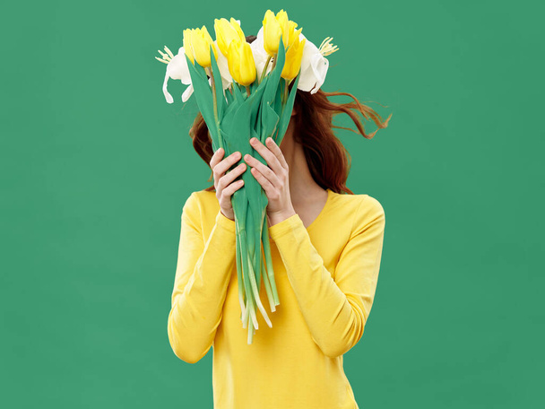 Frau mit Blumenstrauß vor dem Gesicht auf grünem Hintergrund und gelbem Pullover-Modell - Foto, Bild