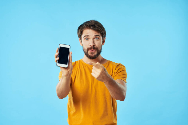 homem com telefone celular gesticulando com as mãos em um fundo azul Copiar espaço - Foto, Imagem