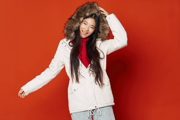 hermosa mujer morena con apariencia asiática en una chaqueta caliente con una capucha sobre un fondo rojo - Foto, imagen