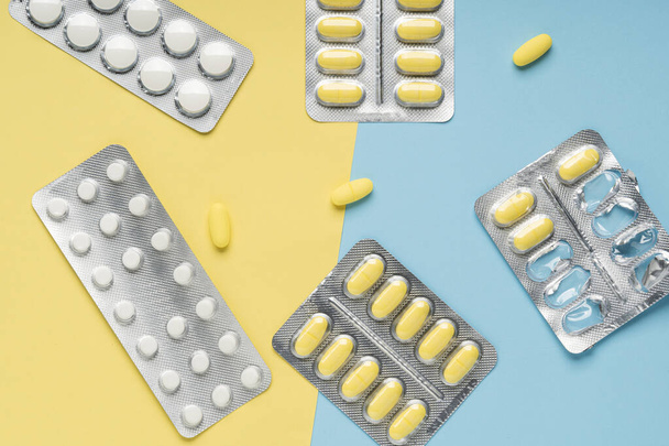 Pilules jaunes et blanches sur fond bleu et jaune, vue de dessus. Différents médicaments, comprimés, capsules médicinales. Concept de médecine, contexte. Pose plate. - Photo, image