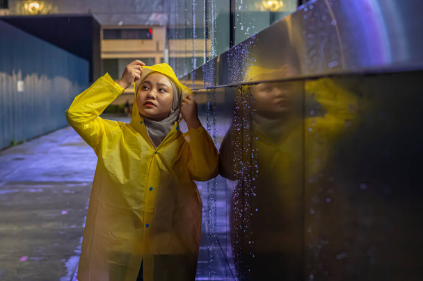 Carino ragazza asiatica indossa cappotto giallo pioggia durante la giornata di pioggia morbida concentrandosi sulla fotografia a bassa luce - Foto, immagini