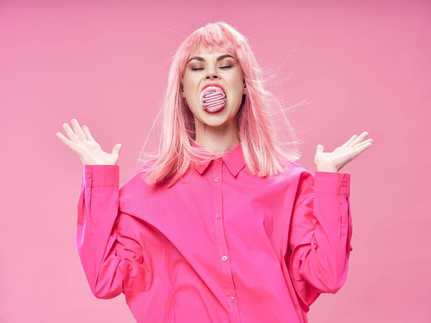 woman in pink wig eating cake and gesturing with hands over isolated background - Фото, зображення