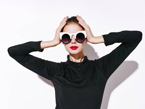жінка модель в чорному светрі і сонцезахисних окулярах тримає її руки на голові
 - Фото, зображення