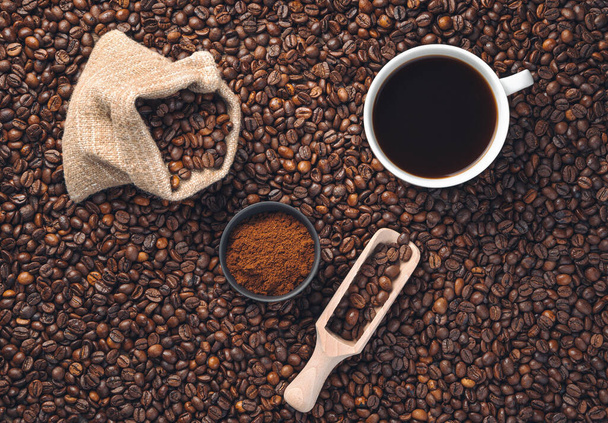 Egy csésze kávé, egy vászonzsák kávé és őrölt kávé a háttérben szétszórt kávébabbal. Felülnézet, másolás. - Fotó, kép