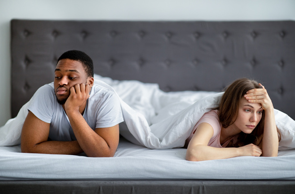 Wütende junge Frau und ihr Mann liegen getrennt auf dem Bett, fühlen sich wütend und beleidigt und blicken in entgegengesetzte Richtungen - Foto, Bild