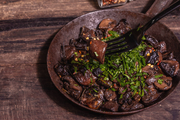 Fried royal champignons in an old cast-iron skillet. Trendy hard light, dark shadow. Vintage wooden table, rustic food style concept, close up - Foto, Imagem