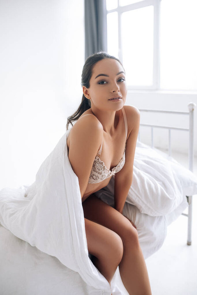 Приваблива сексуальна жінка сидить в ліжку, загорнута в ковдру і посміхається
. - Фото, зображення