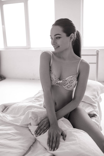 Ελκυστική σέξι γυναίκα κάθεται στο κρεβάτι με δαντελωτά εσώρουχα. Ασπρόμαυρη εικόνα. - Φωτογραφία, εικόνα