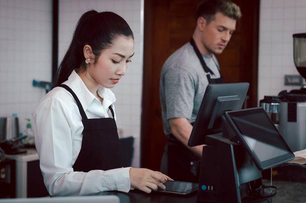 Mladá žena a muž barista nosí zástěru stojící za kavárnou pokladní pult, servírka a číšník personál pracující v kavárně. - Fotografie, Obrázek