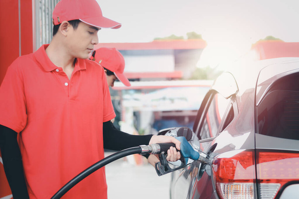 Pracownik stacji benzynowej w czerwonym mundurze trzymający dyszę pompy paliwa przed tankowaniem paliwa na stacji benzynowej. - Zdjęcie, obraz