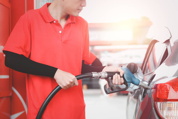 Benzinestation in rood uniform met een tankpompmondstuk tegen voor het tanken van de auto bij het benzinestation. - Foto, afbeelding
