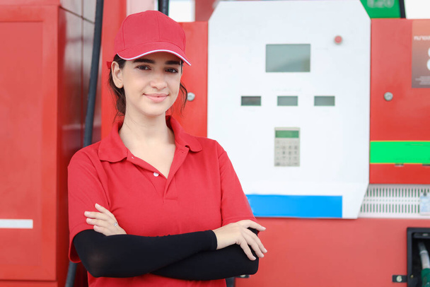Porträt einer glücklich lächelnden schönen Tankstellenwärterin in roter Uniform, die mit verschränkten Armen an der Tankstelle steht. - Foto, Bild