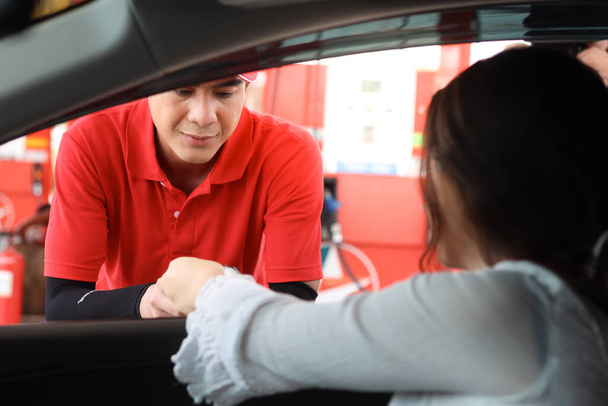 Junger asiatischer Tankwart in roter Uniform vor dem Autofenster, der Kreditkarte (Attrappe) vom Kunden zur Bezahlung an der Tankstelle bekommt. - Foto, Bild