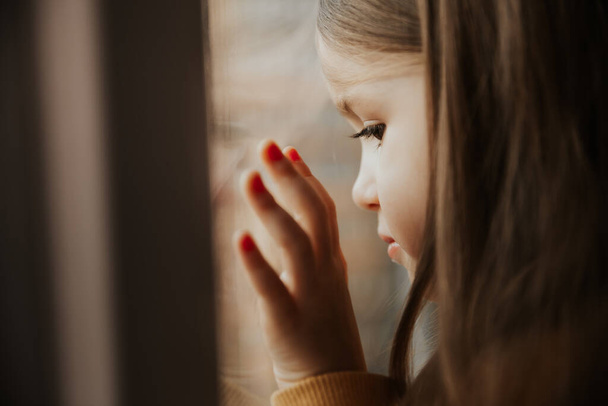 little girl looks out the window of a high-rise building in a sleeping area leaning her face against the glass - Photo, Image