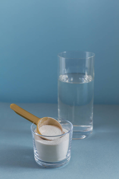 Collagen powder in bowl, glass of water and measure spoon on light blue background - Foto, Imagen