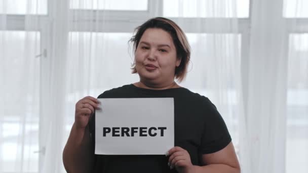 Concept lichaam positiviteit - een mollig lachende vrouw houdt een bord met de inscriptie PERFECT - kijken in de camera - Video