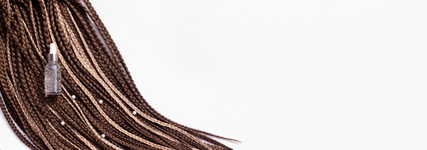Banner. Thin brown African braids and a jar of care oil on a white background. Hair close-up, braided dreadlocks, afro style - Photo, Image
