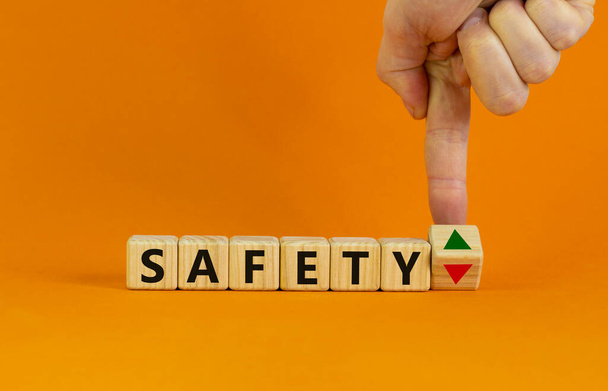 Safety level symbol. Businessman turns a cube and changes the expression 'safety down' to 'safety up'. Beautiful orange background. Business, safety level concept. Copy space. - Foto, afbeelding