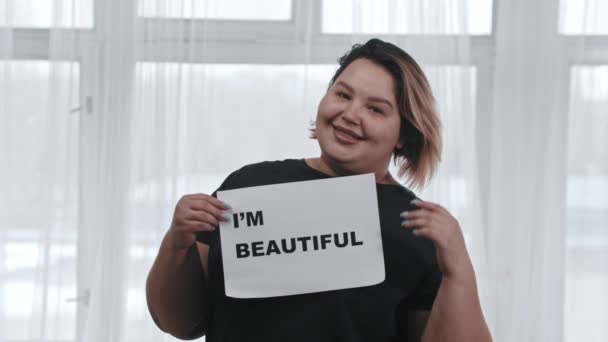 Koncepció test pozitivitás - kövér nő tartja a jelet a felirat IM BEAUTIFUL - belenéz a kamerába - Felvétel, videó