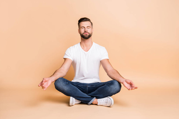 Portrait of nice calm focused guy sitting on floor meditating relaxation isolated over beige pastel color background - Foto, Bild