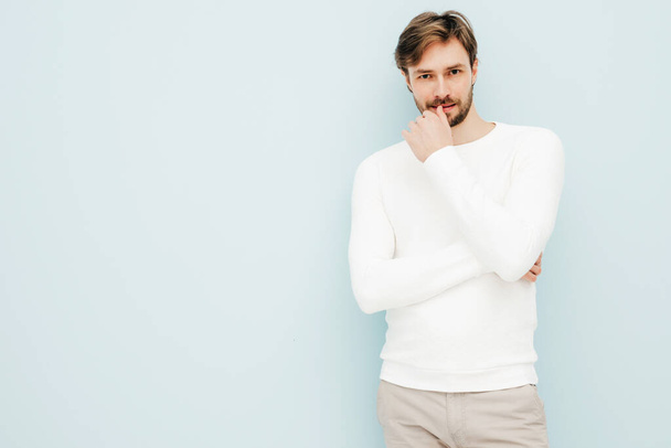 Portrait of handsome smiling hipster lumbersexual businessman model wearing casual white sweater and trousers. Fashion stylish man posing against light blue wall in studio - Φωτογραφία, εικόνα