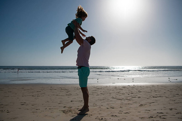 Father throws son up against the blue sky. Dad throwing child. Handsome man father carrying young boy son. Happy dad holding child. Lifestyle and family vacation, happiness men concept. - Foto, Imagen