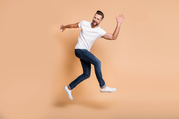Full length body size view of attractive funky cheerful guy jumping having fun dancing running isolated over beige pastel color background - Valokuva, kuva