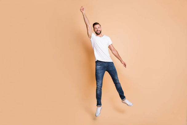 Full length body size view of nice funky cheerful guy jumping holding invisible parasol isolated over beige pastel color background - Foto, Imagen