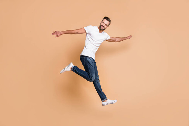 Full length body size view of nice cheerful guy jumping having fun good mood isolated over beige pastel color background - Photo, Image
