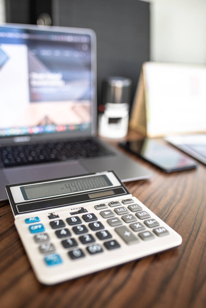 close-up calculator tegen de achtergrond van de laptop op het bureaublad - Foto, afbeelding