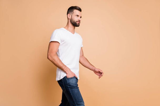 Profile side view portrait of attractive serious macho guy walking copy space isolated over beige pastel color background - 写真・画像