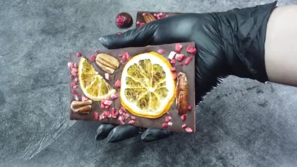 A kézműves csokoládé a kezedben van. Közelkép luxus kézzel készített csokoládé fűszerekkel, száraz bogyókkal és dióval. - Felvétel, videó