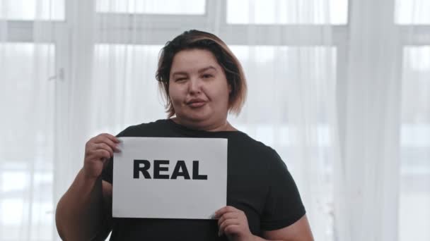 Koncepcja pozytywności ciała - tłusta, charyzmatyczna kobieta trzyma napis REAL - patrząc w kamerę - Materiał filmowy, wideo