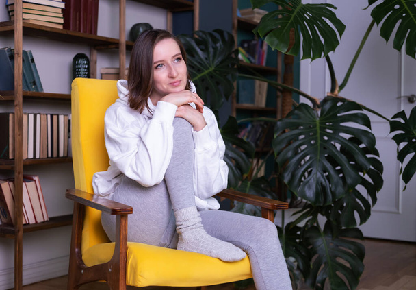 Young beautiful woman in casual clothes sitting on yellow couch in modern interior - Photo, Image