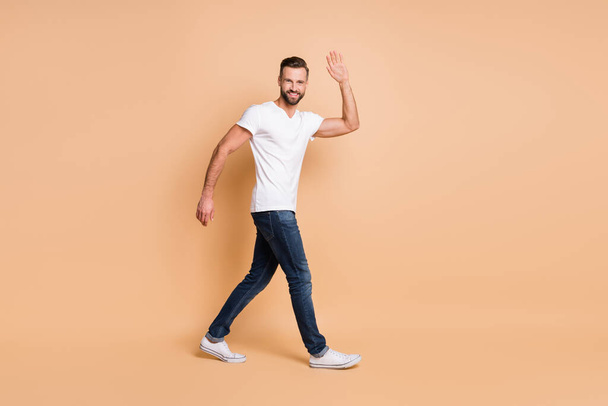 Full body profile side photo of young man happy positive smile wave hi hello go walk isolated over beige color background - Фото, зображення