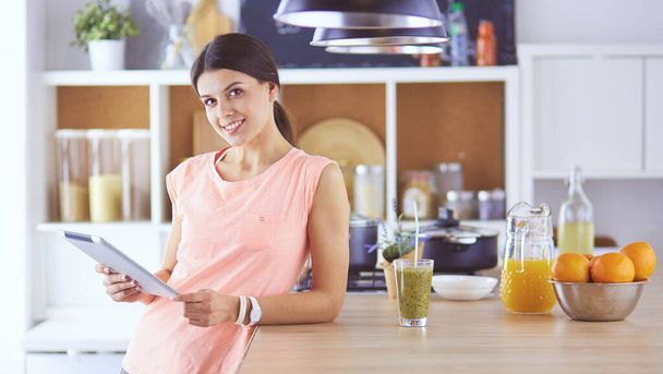 Beautiful young woman using a digital tablet in the kitchen - Photo, Image