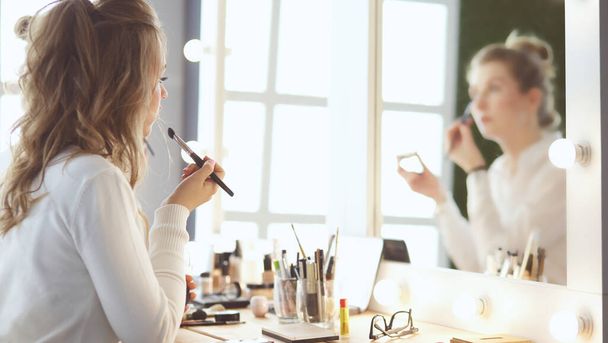 Make-up artist applying white eyeshadow in the corner of models eye and holding a shell with eyeshadow on background - Foto, Bild